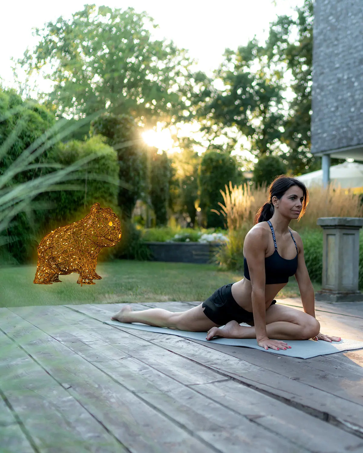 Leuchtende Tierfigur aus Draht als dekoratives Lichtobjekt im Garten – neben einer Frau beim Yoga bei Sonnenuntergang.