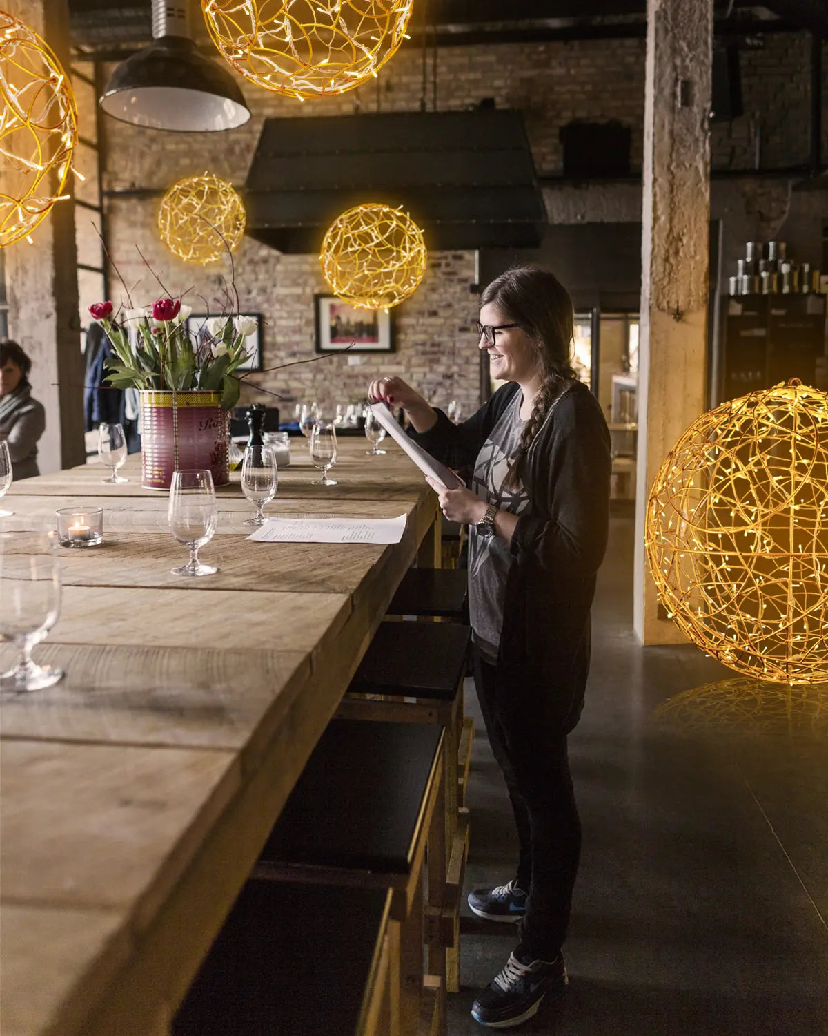 Goldene Kugel-Lichtobjekte in einer Bar mit industriellem Ambiente – leuchtende Drahtskulpturen schaffen warme Atmosphäre über einem Holztresen.