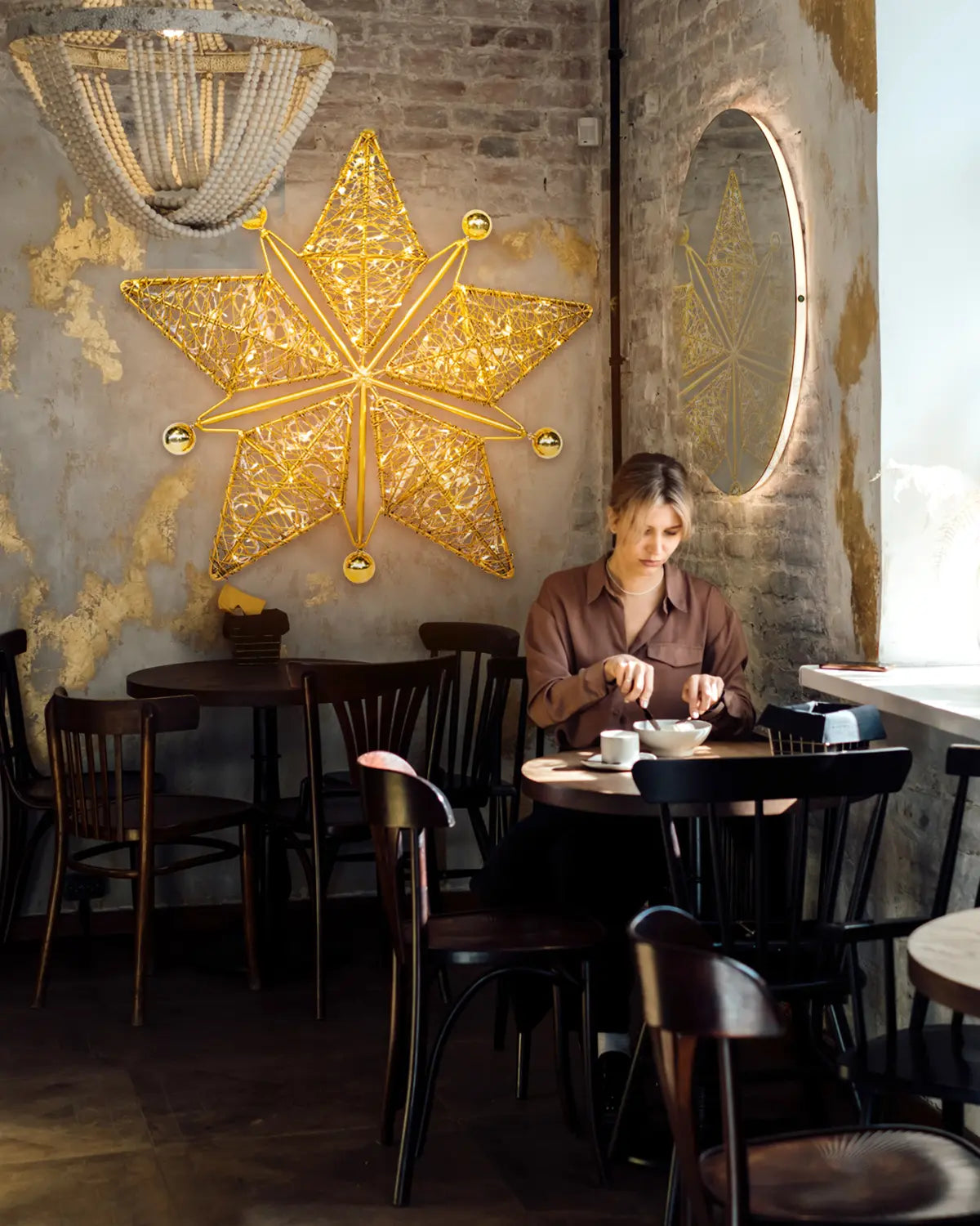 Achtzackiger goldener Wandstern von Alganic in urbanem Café – dekorative Lichtskulptur mit ruhiger, stimmungsvoller Präsenz.