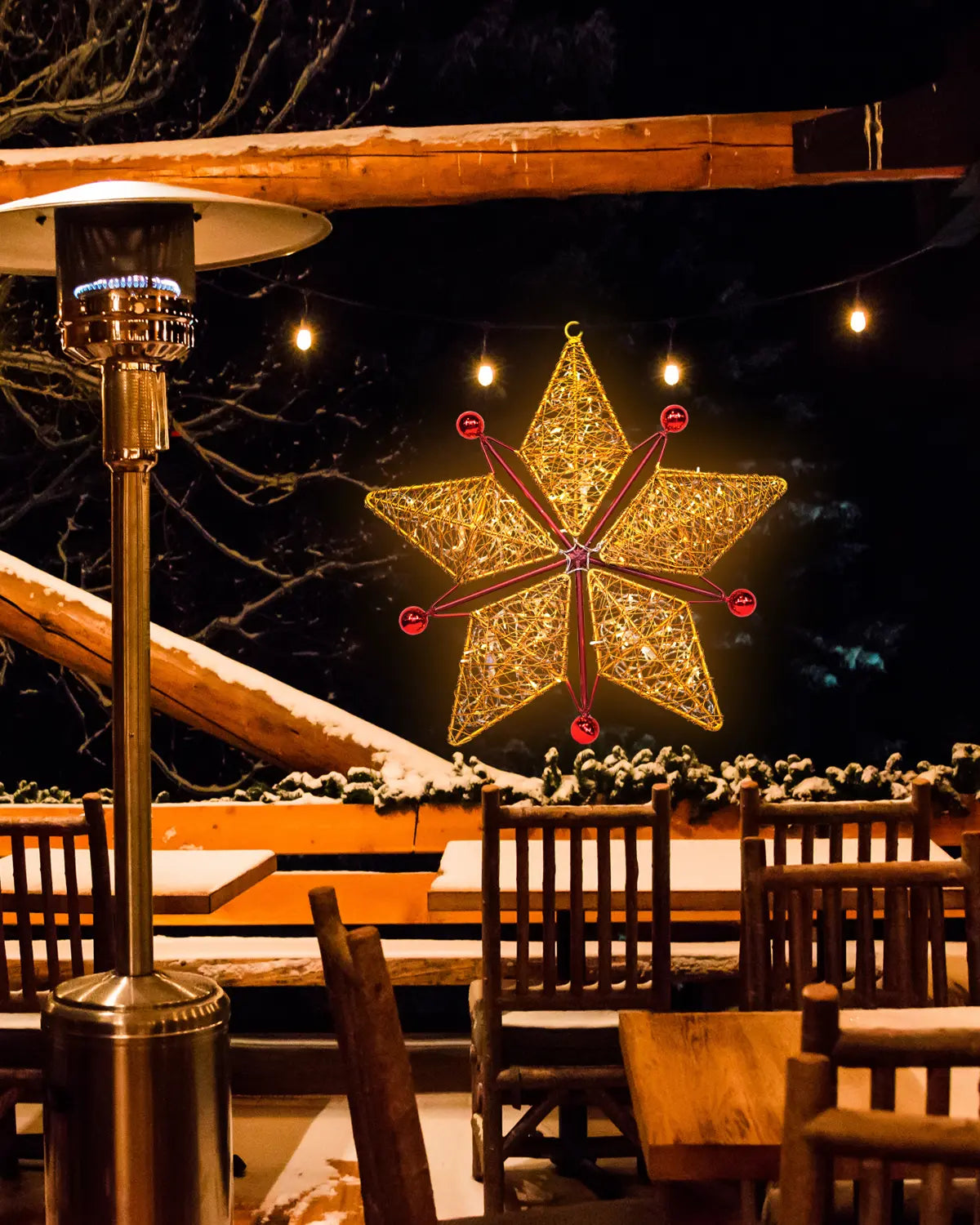 Goldener Weihnachtsstern im Außenbereich eines verschneiten Lokals – leuchtende Drahtstruktur mit ruhiger Wirkung. / Golden Christmas star outside a snowy restaurant terrace – glowing wire object with quiet presence.