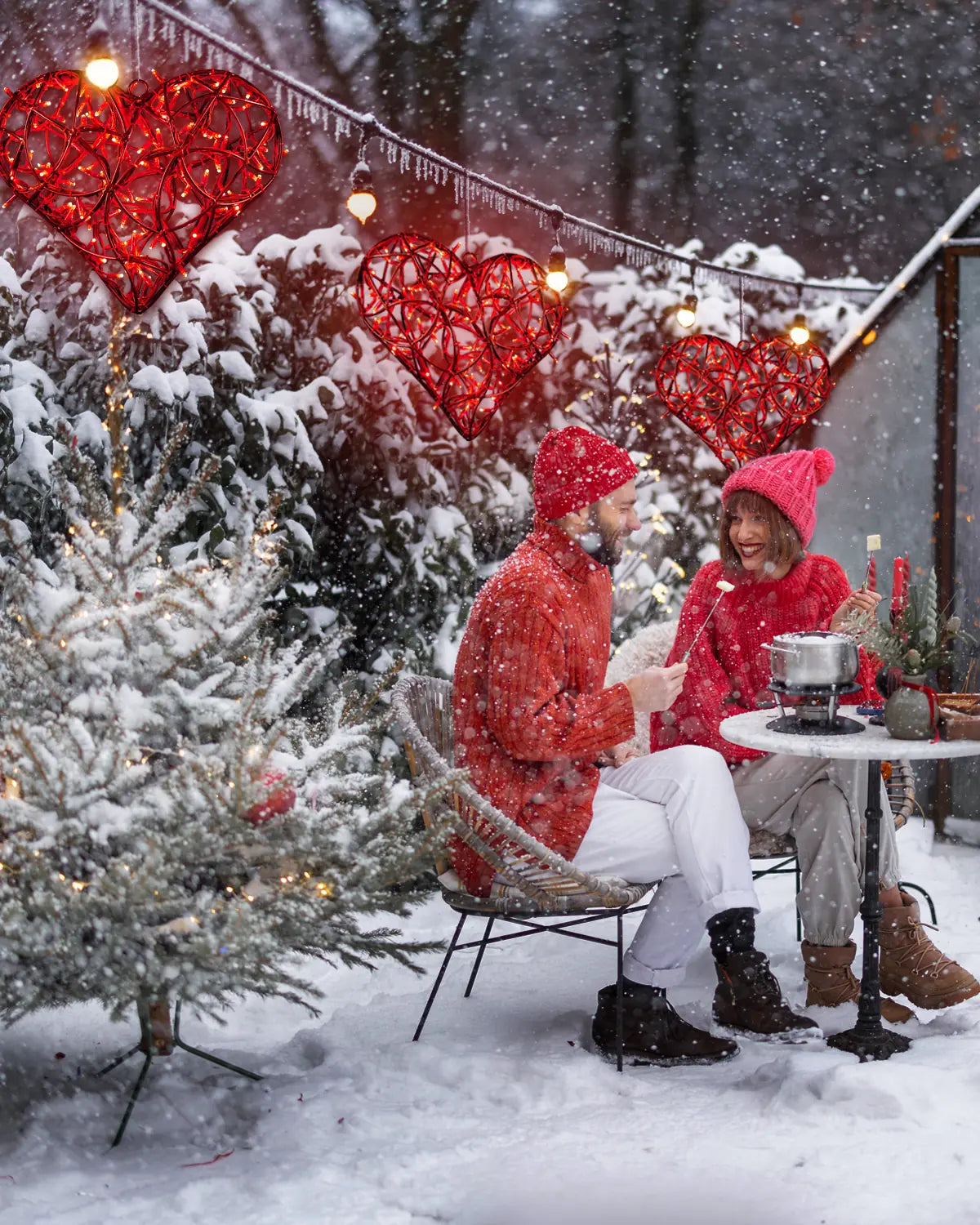 Rote Herz-Lichtobjekte als hängende Dekoration im verschneiten Außenbereich – winterliches Fondue-Setting mit romantischer Stimmung.