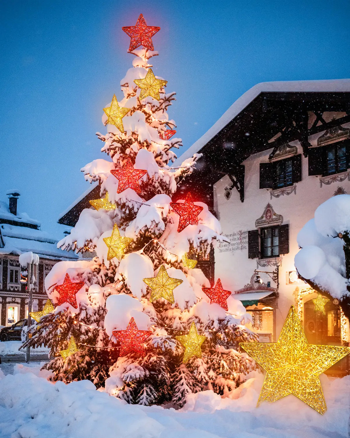Geschmückter Weihnachtsbaum mit roten und goldenen Alganic-Sternen – leuchtende Installation im verschneiten Ortszentrum.