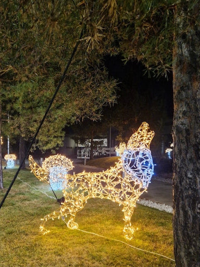 Leuchtender Wolf mit blauer Brustzone – winterliche Außenskulptur aus Licht, installiert im Parkbereich unter Bäumen.